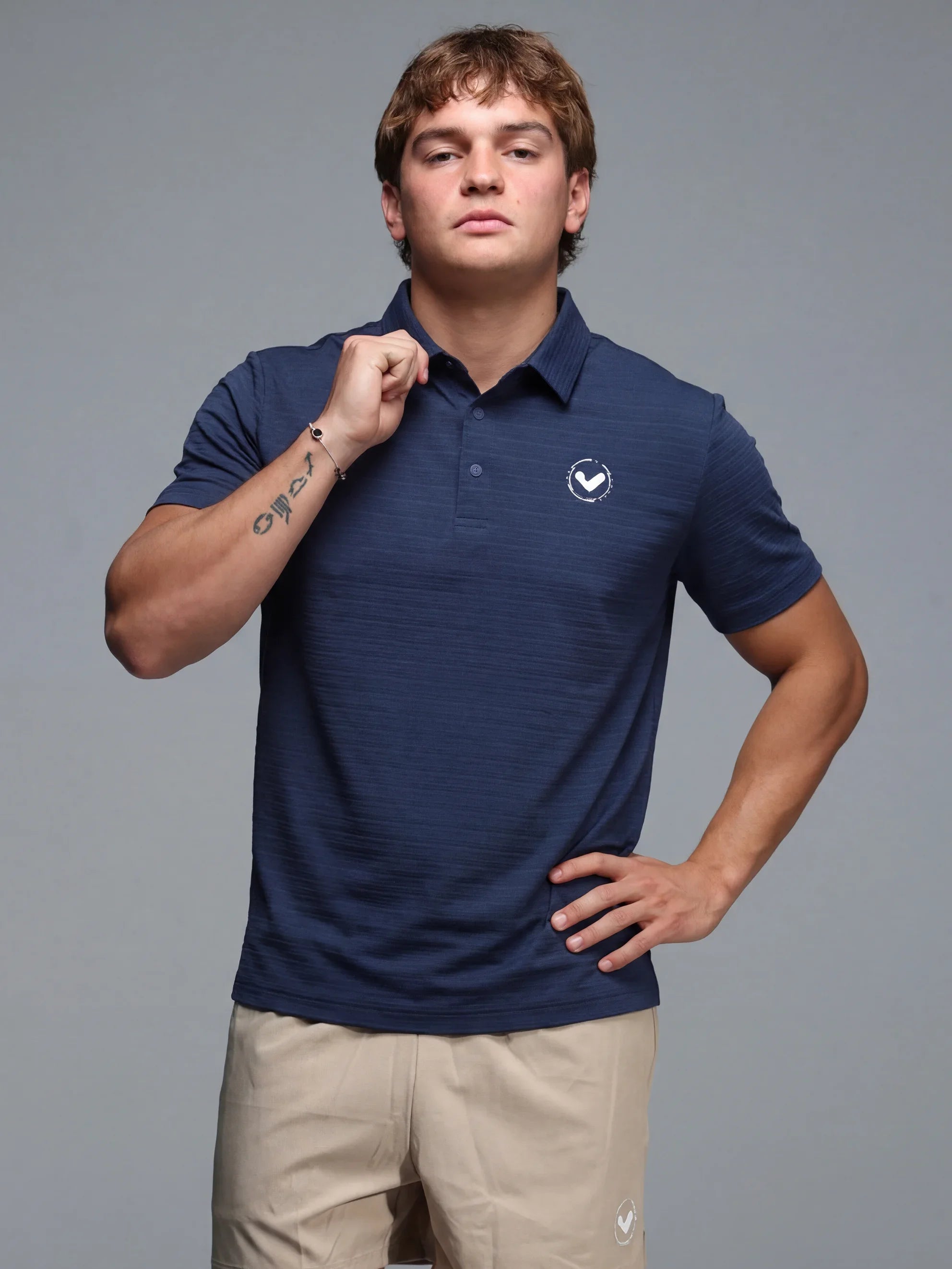 Man wearing a navy blue polo shirt with a logo on a gray background