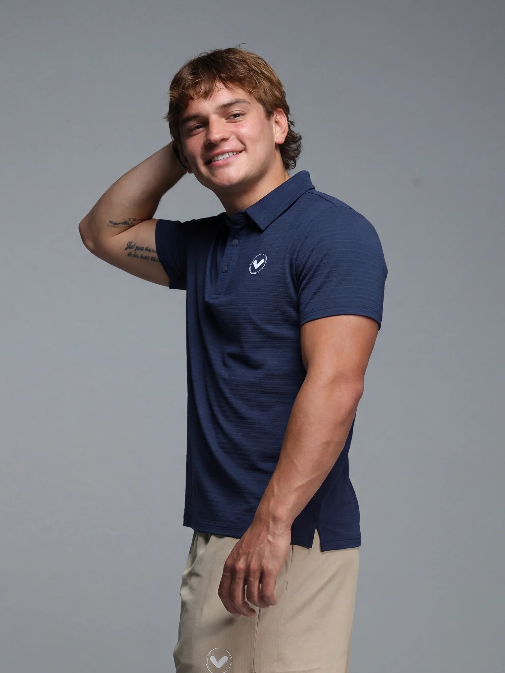 Man wearing a navy blue Nike polo shirt and beige shorts against a gray background