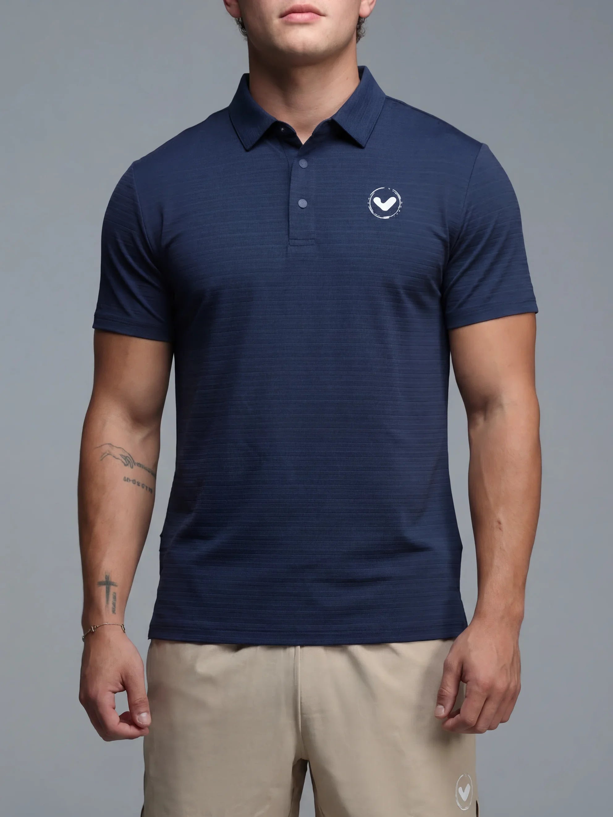 Man wearing a navy blue polo shirt and beige shorts on a gray background