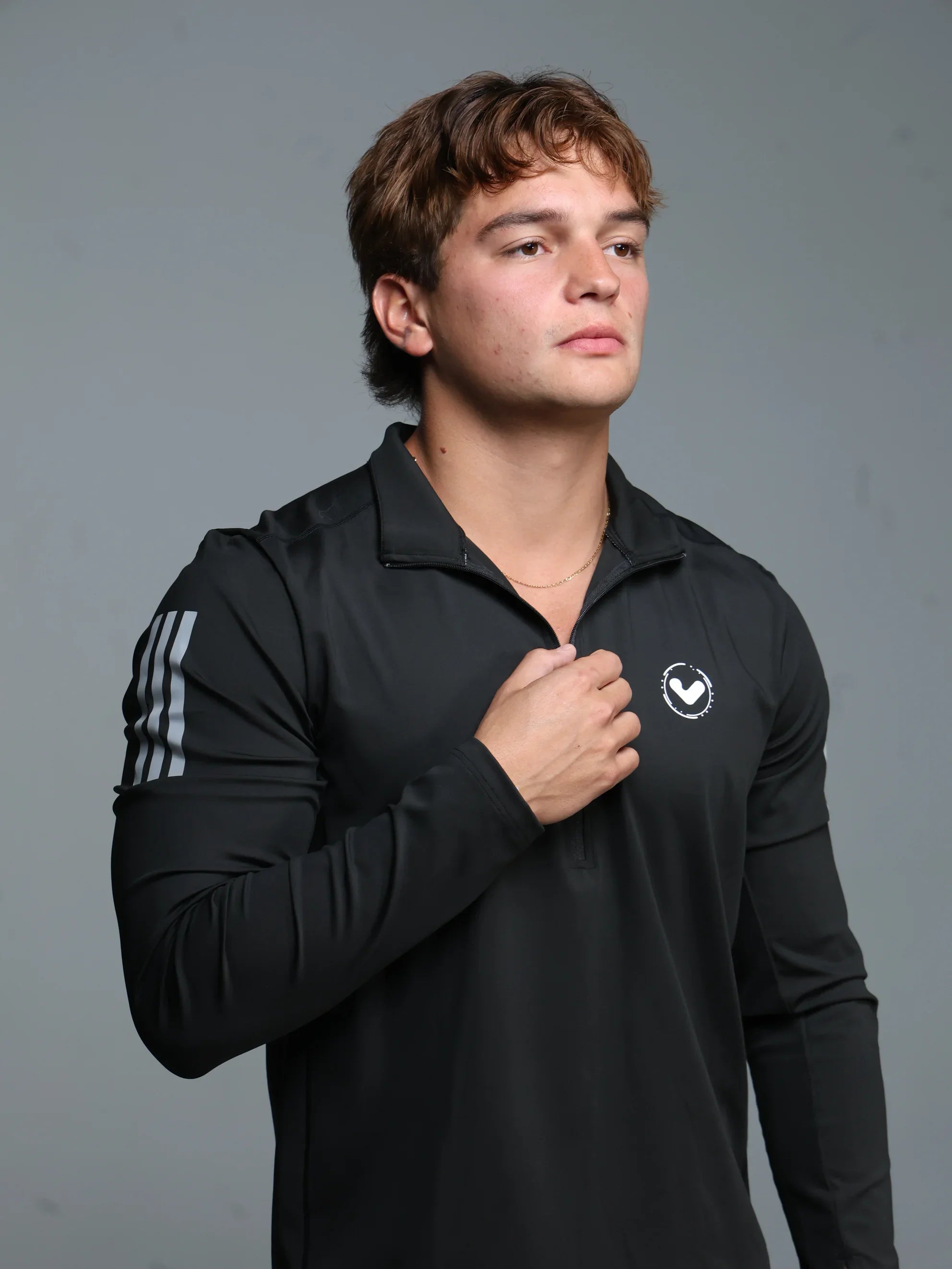 Person wearing a black athletic jacket with logos on a gray background