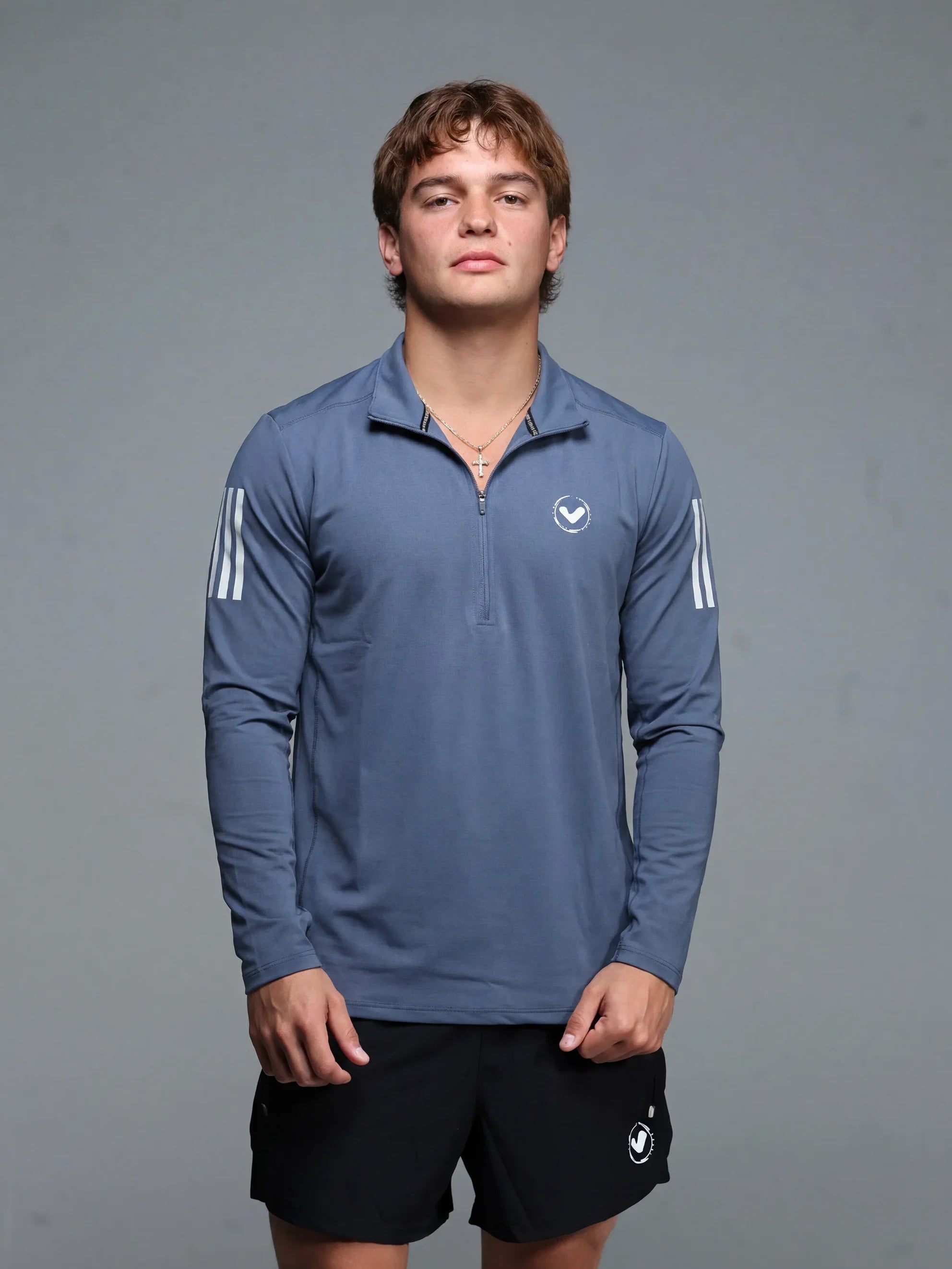Person wearing a blue athletic long-sleeve shirt with white stripes and black shorts on a gray background