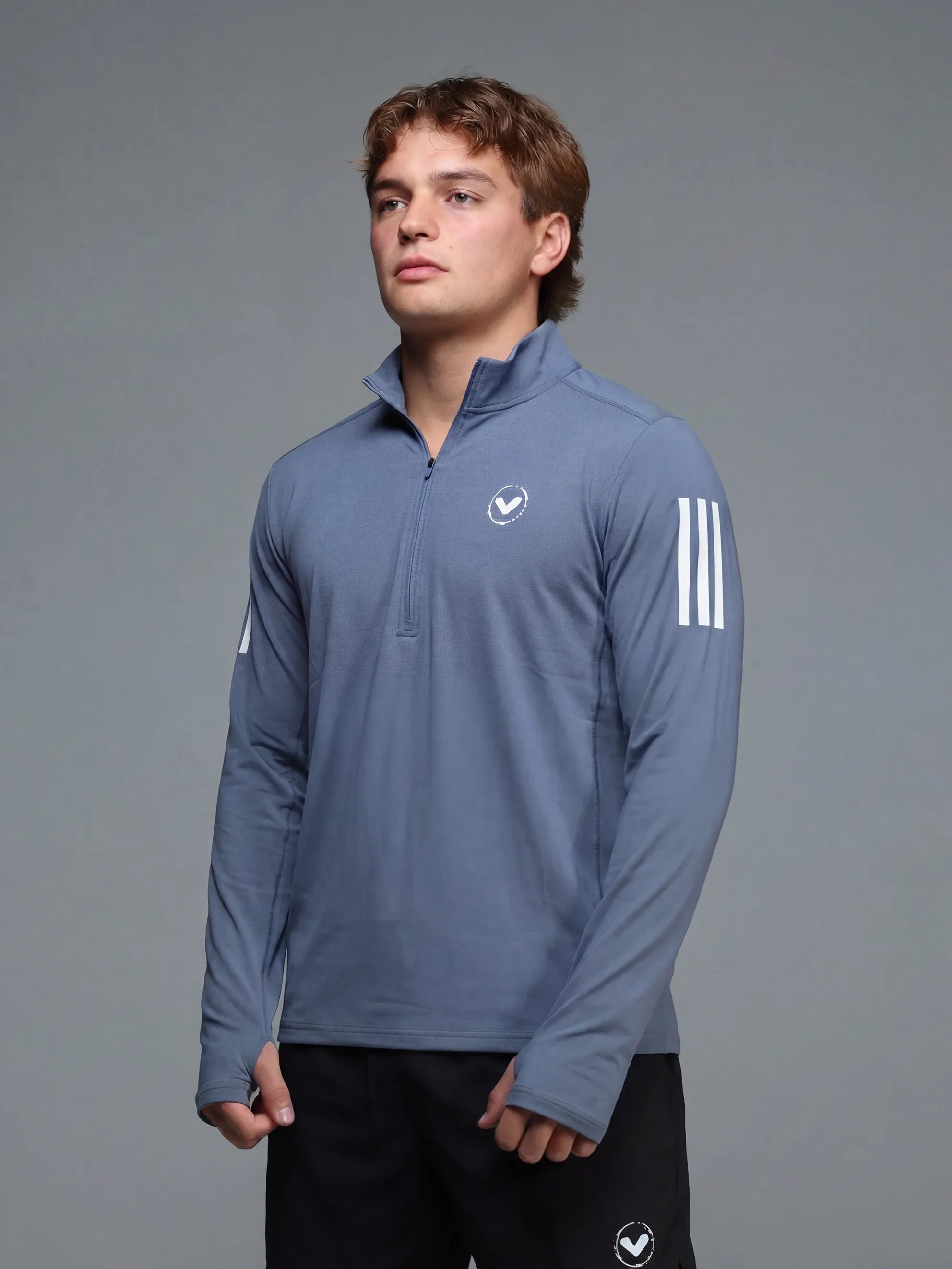Man wearing a blue athletic long-sleeve shirt with a logo on a gray background