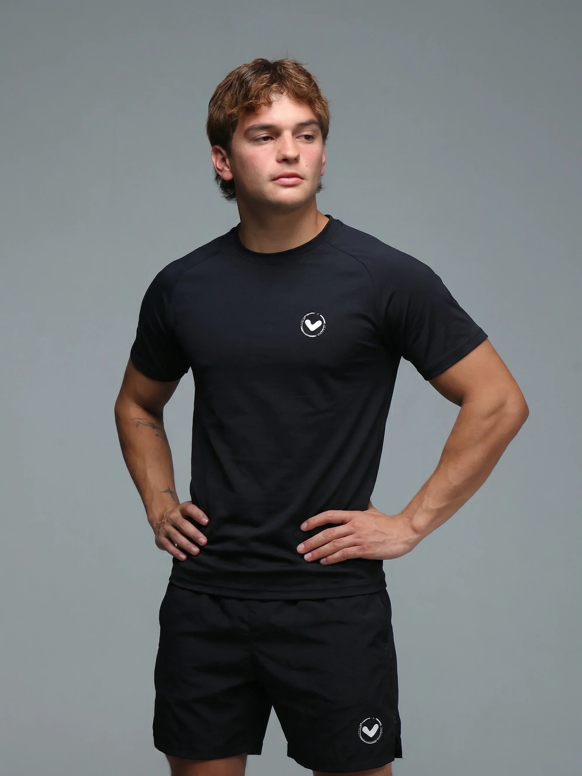 Man wearing a black t-shirt and shorts with a logo on a gray background