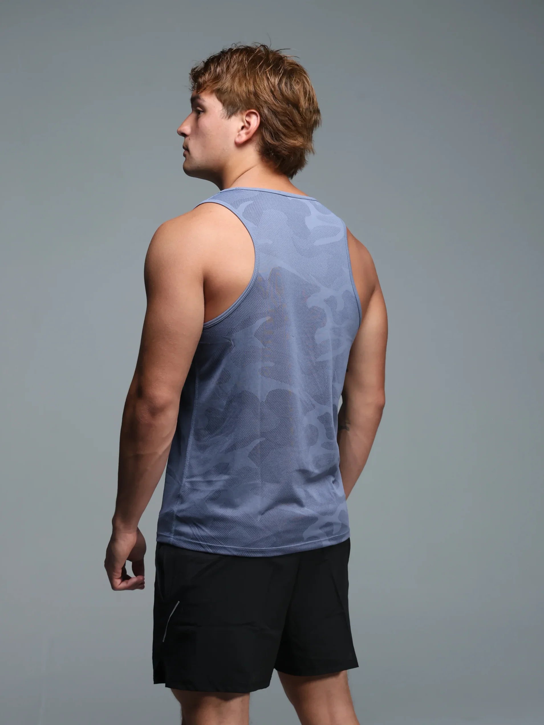 Man wearing a light blue sleeveless shirt and black shorts on a gray background