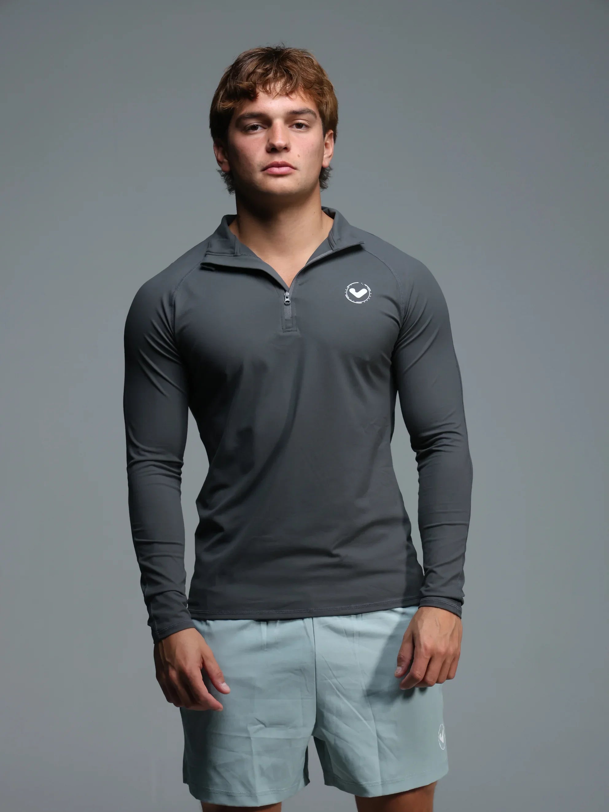 Man wearing a gray long-sleeve athletic shirt with a logo on a gray background