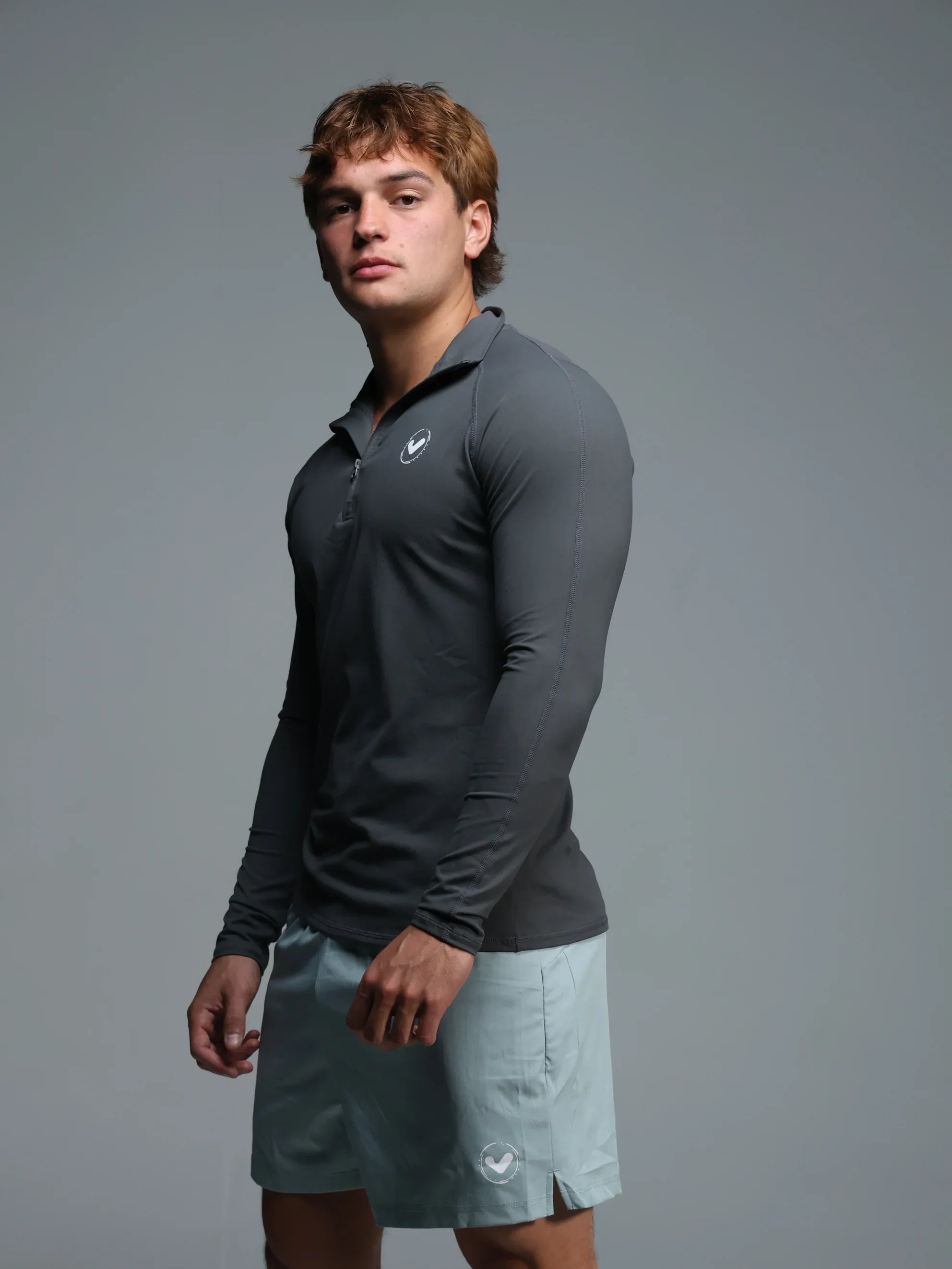 Man wearing a dark gray long-sleeve polo shirt and light gray shorts on a gray background