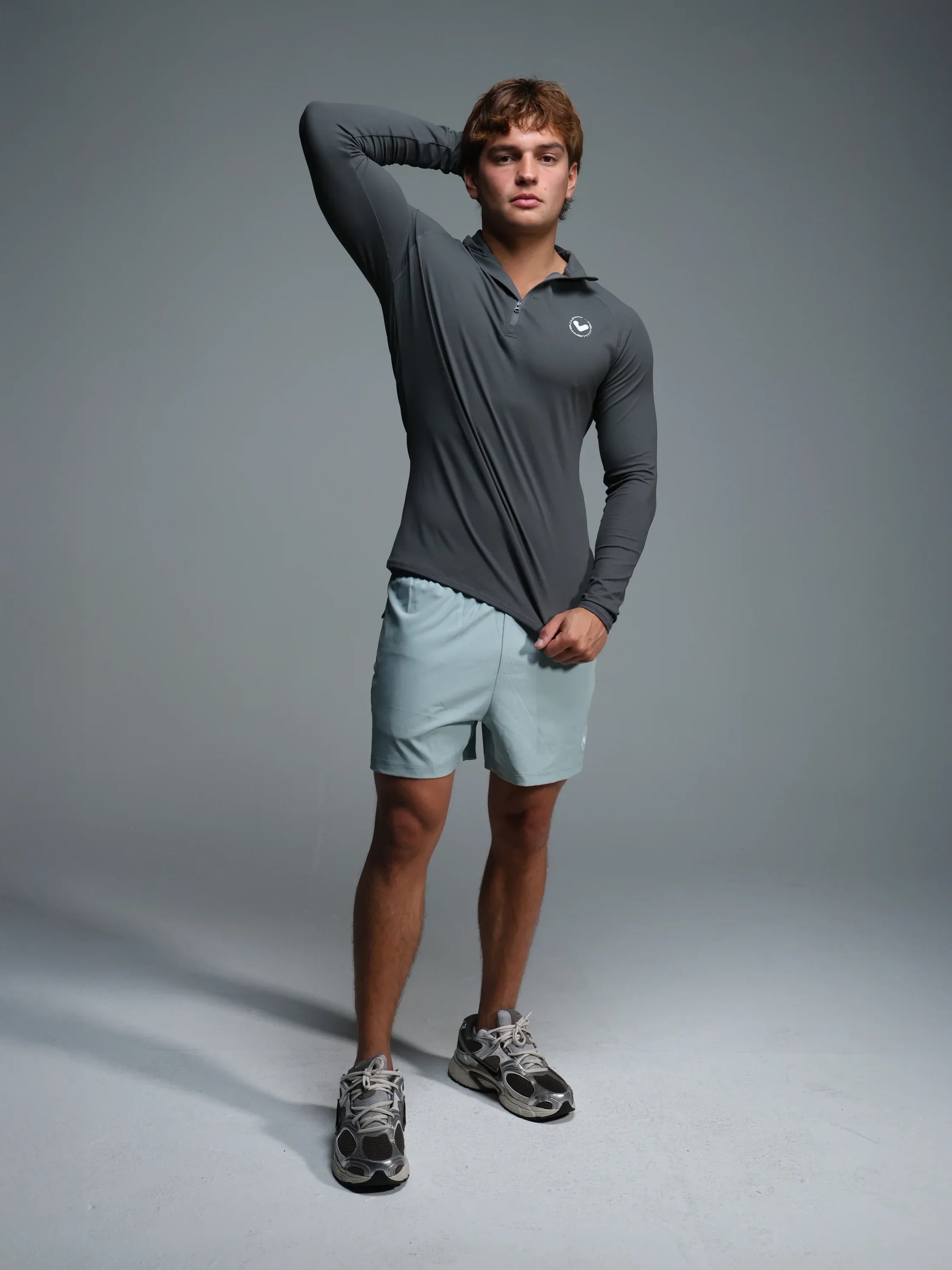 Man wearing a gray long-sleeve shirt and light blue shorts on a gray background