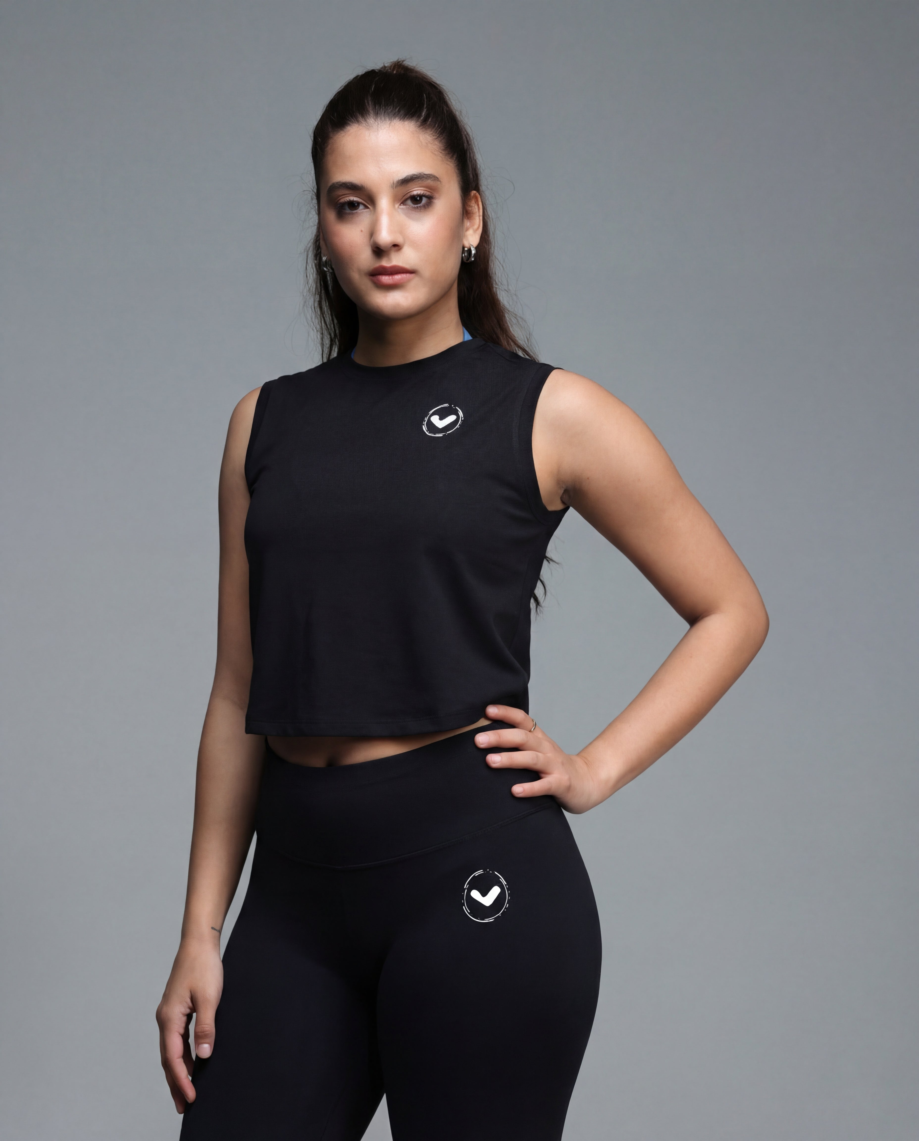Woman wearing a black sleeveless top and leggings with a logo on a gray background