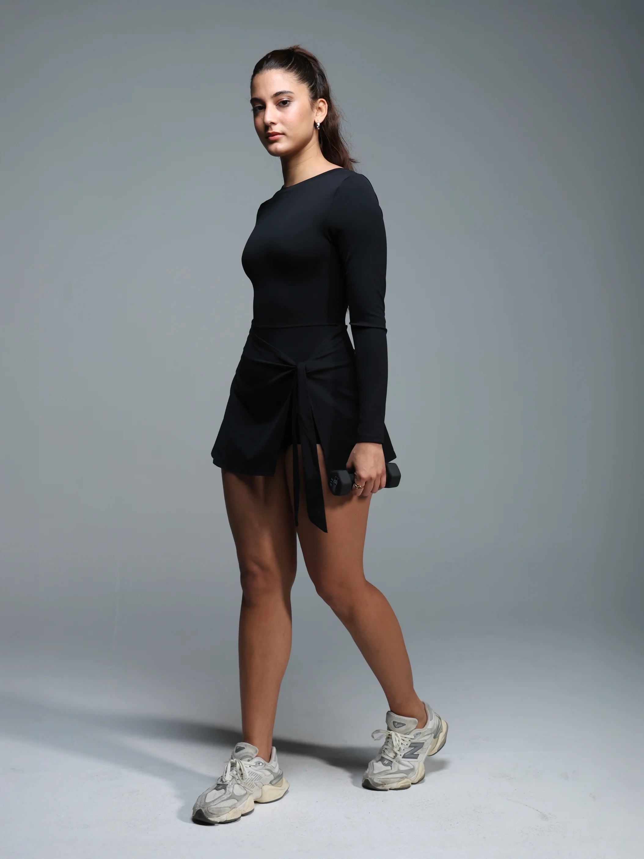 Woman in black athletic wear holding dumbbells against a gray background