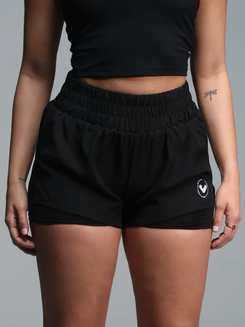 Person wearing black athletic shorts with a logo on a gray background
