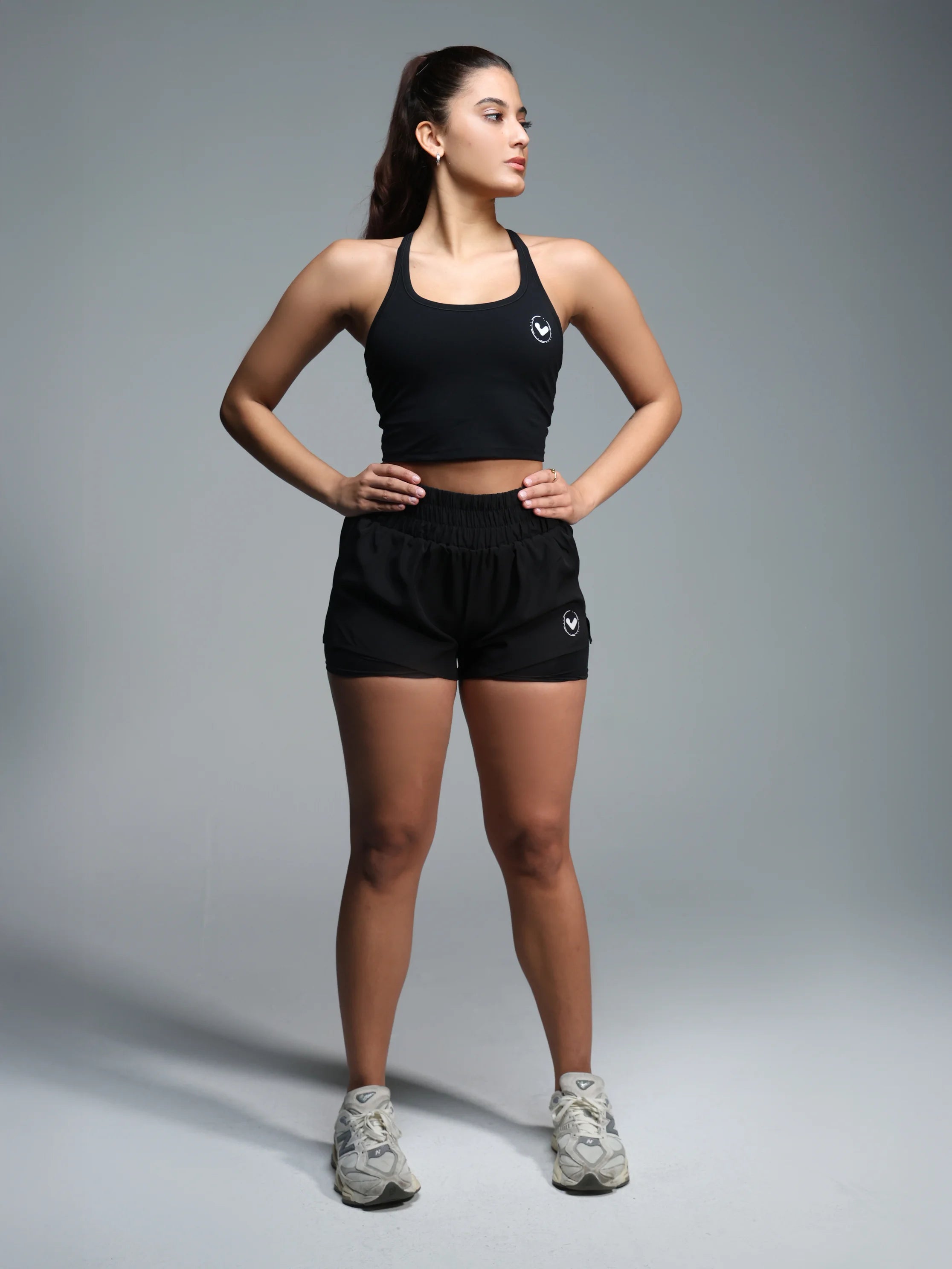 Woman wearing a black athletic outfit with a logo on a gray background
