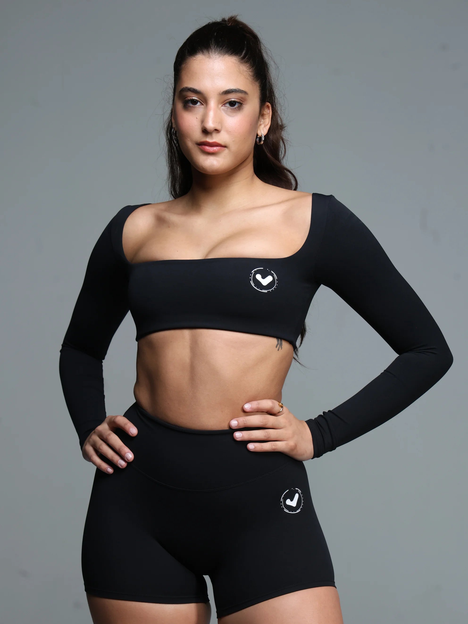 Woman wearing a black athletic outfit with a logo on a gray background