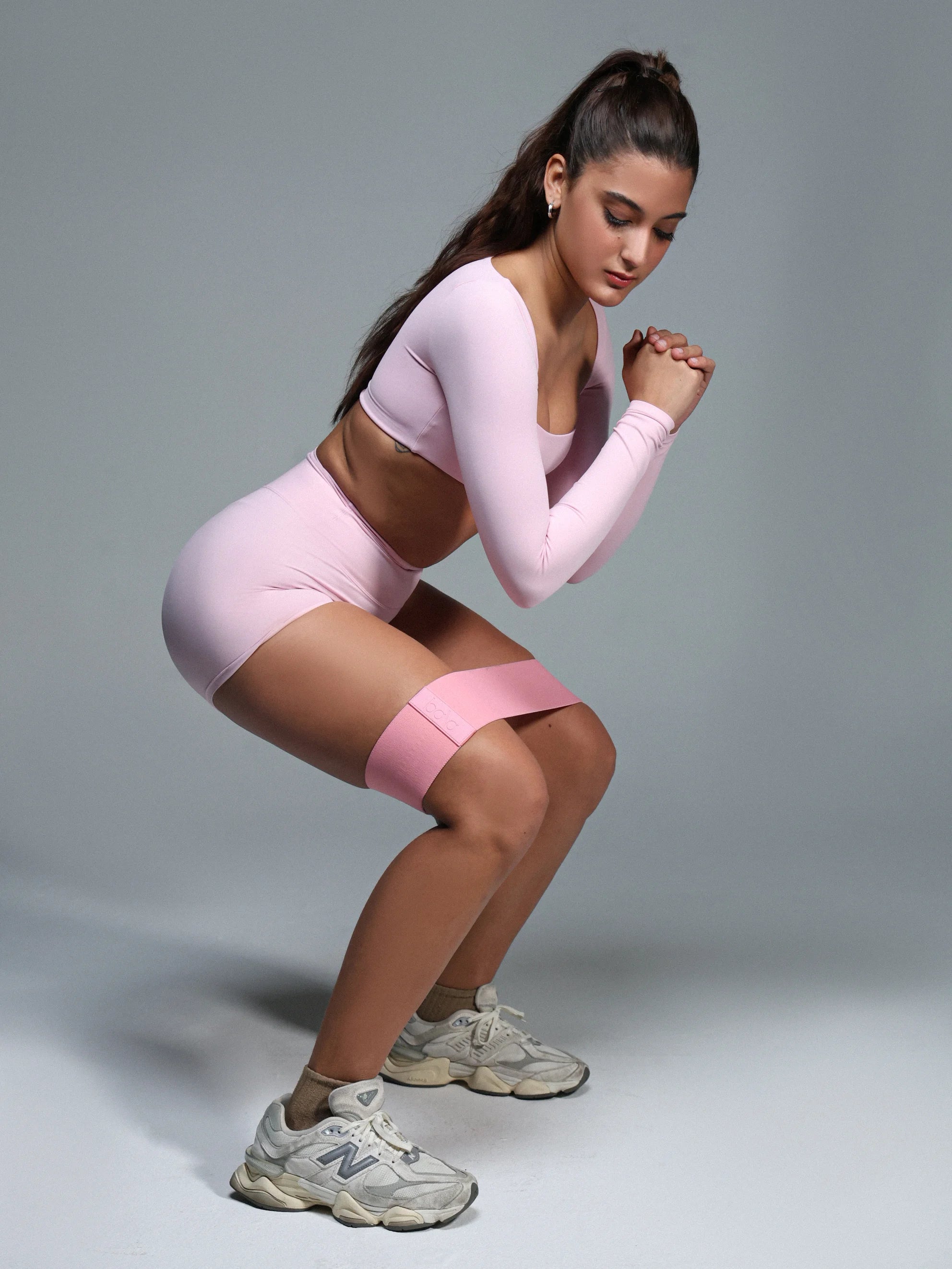 Woman in pink athletic wear performing a squat against a gray background
