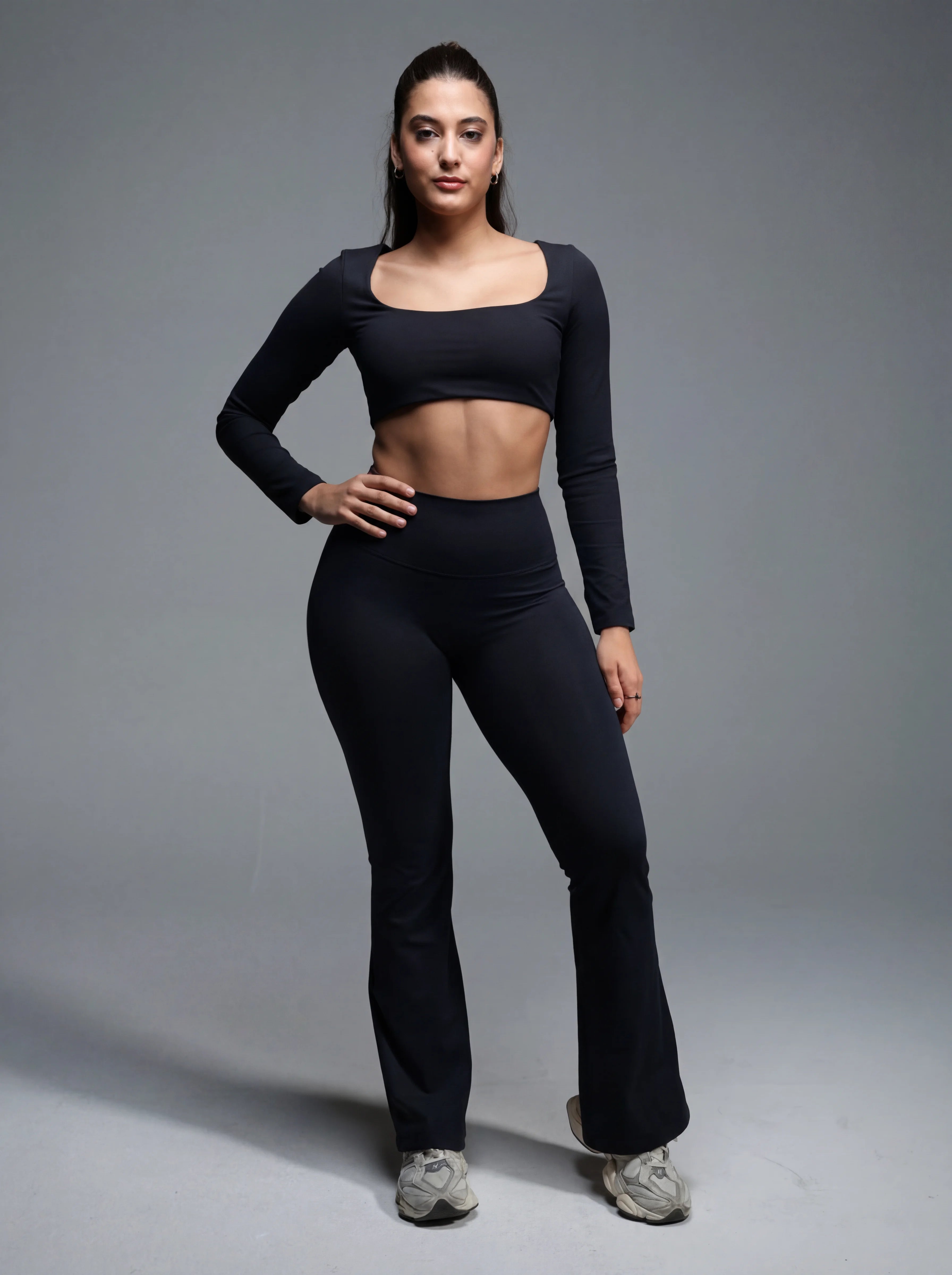 Woman wearing a black long-sleeve top and black leggings on a gray background