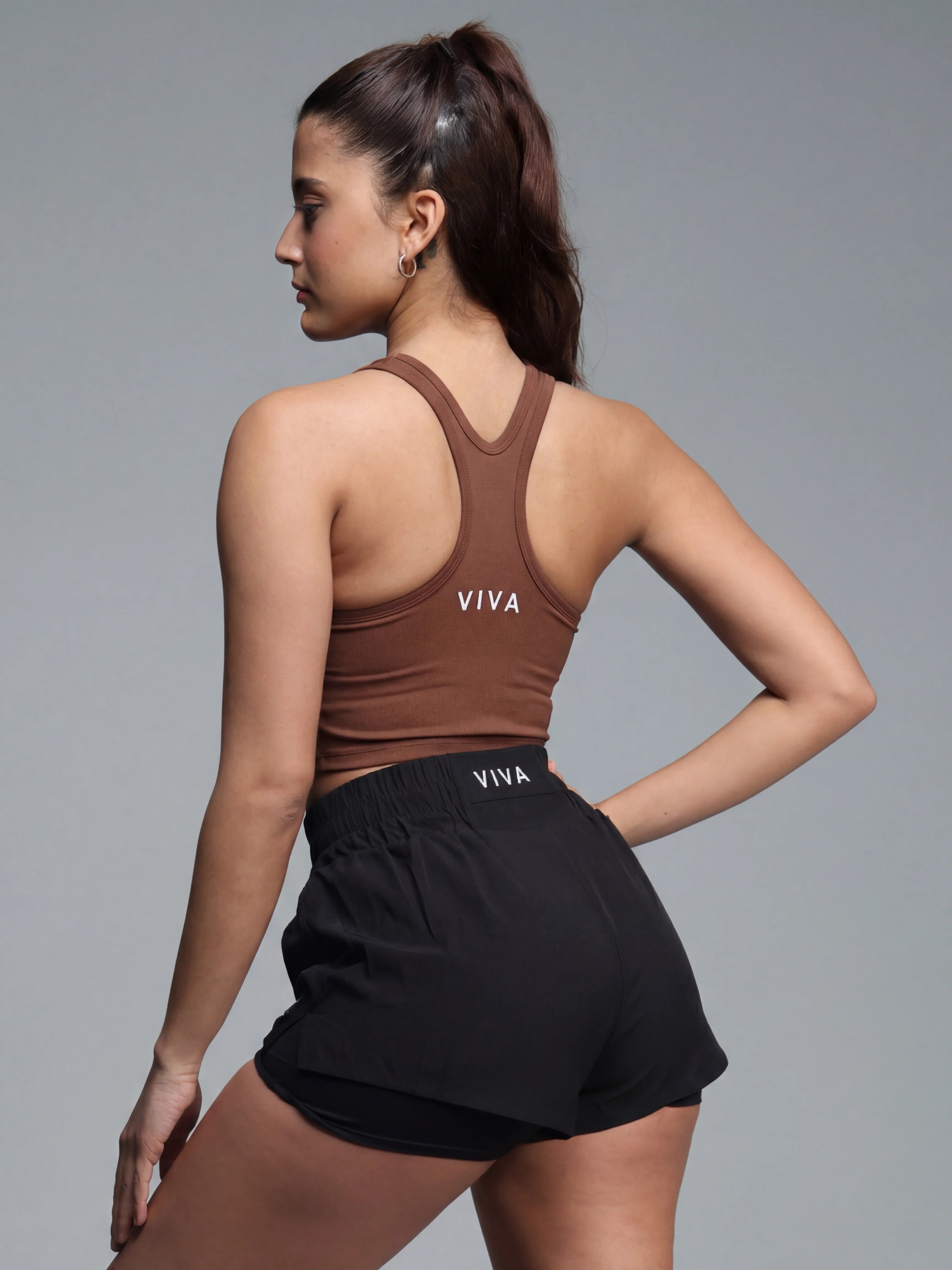 Woman wearing a brown tank top and black shorts with 'VIVA' branding on a gray background